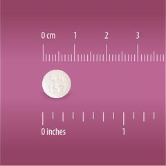 A small round white uncoated Globe Aspirin 325mg tablet (NSAID pain reliever) is shown on a pink background next to rulers in centimeters and inches, highlighting its size; commonly used for pain and fever relief.
