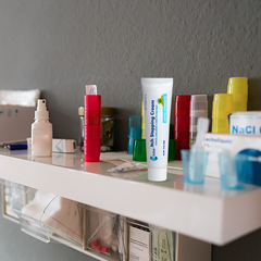 A white shelf against a gray wall holds various medical supplies, including bottles and containers, a tube labeled "Nail Stopping Cream," and Globe Anti-Itch Cream with Histamine Blocker (Compare to BENADRYL), 1.5 oz, by Globe.