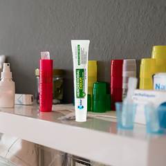 A 1.8 oz tube of Globe Hemorrhoid Symptom Treatment Cream, Pain Relief with Aloe, stands upright on a bathroom shelf among colorful cups and toiletries, set against a gray wall.