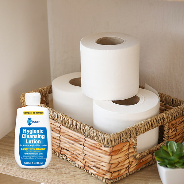 A wicker basket holds three toilet paper rolls on a shelf. Next to it is TriSelfcare Globe Hygienic Cleansing Lotion, a 3oz gentle cleanser for sensitive areas that soothes pain and itch—compare to Balneol—for men and women.