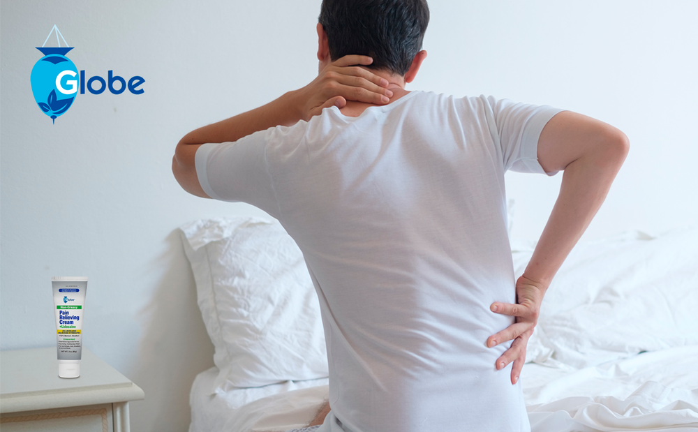 A person in a white shirt sits on a bed, holding their neck and lower back in pain. A 3 oz tube of Globe Pain Relieving Cream Plus 4% Lidocaine, fast-acting and unscented, is visible to the left with the Globe logo.