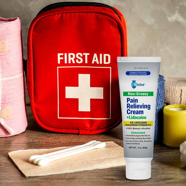 A tube of Globe Pain Relieving Cream Plus 4% Lidocaine (3 oz) sits on a wooden surface with a red first aid kit, cotton swabs, rolled bandages, and medical tape for fast-acting numbing relief.