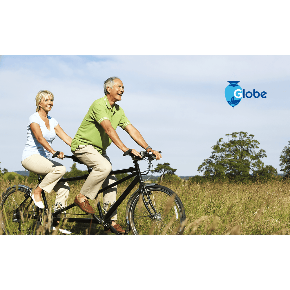 A happy older couple rides a tandem bike through a sunny, grassy field—enjoying relief from discomfort thanks to Globe Hemorrhoid Symptom Treatment Cream with Aloe. The Globe logo appears in the upper right against a blue sky.