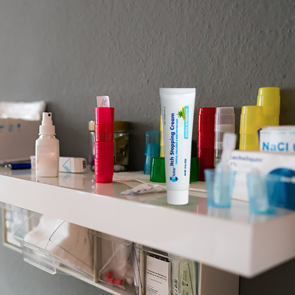 A white shelf against a gray wall holds various medical supplies, including bottles and containers, a tube labeled "Nail Stopping Cream," and Globe Anti-Itch Cream with Histamine Blocker (Compare to BENADRYL), 1.5 oz, by Globe.