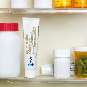 A 1 oz tube of Globe Multi-Action Ointment, an antibiotic pain-relieving first aid ointment with Neomycin, Bacitracin, Pramoxine HCl, and Polymyxin B, stands upright on a cabinet shelf among pill bottles and containers of green and yellow pills.