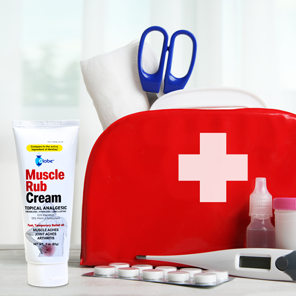 A red first aid kit with a white cross, scissors, gauze, medicine bottles, thermometer, pills, and Globe Ultra Strength Greaseless Muscle Rub Cream (3 oz), featuring 10% menthol and 15% methyl salicylate, is displayed in the foreground.