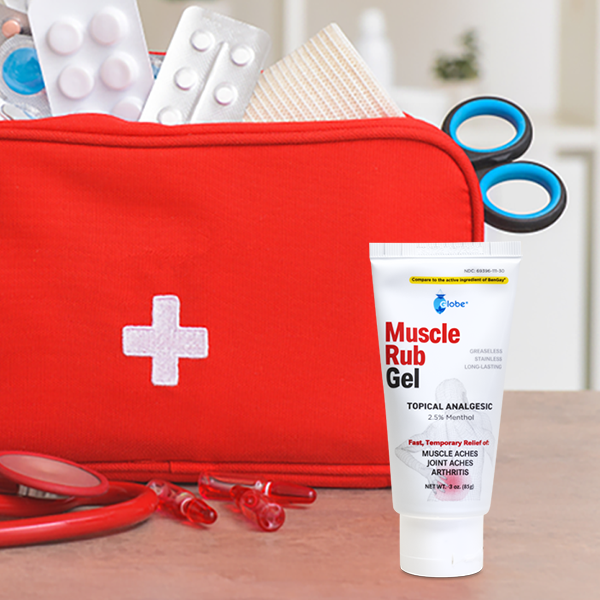 A tube of Globe Muscle & Joint Vanishing Scent Gel (3 oz), a non-greasy pain reliever with 2.5% menthol for muscle, back, and minor arthritis pain, stands in front of a red first aid kit holding scissors, bandages, and blister packs.