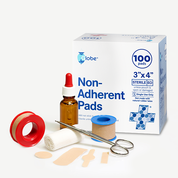 A box of Globe Sterile Non-Adherent Pads, 100-pack (3” x 4”), is pictured on a white background with first aid essentials—including a brown dropper bottle, adhesive tape, gauze, scissors, and assorted bandages.